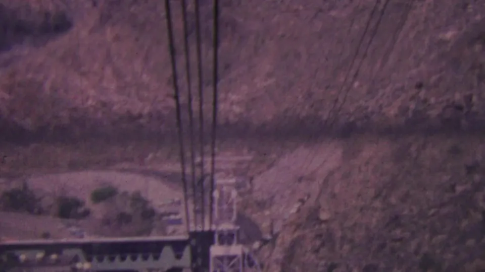 High-angle 1964 Palm Springs tramway view with dark cables crossing a faded desert canyon and a metal support tower below.