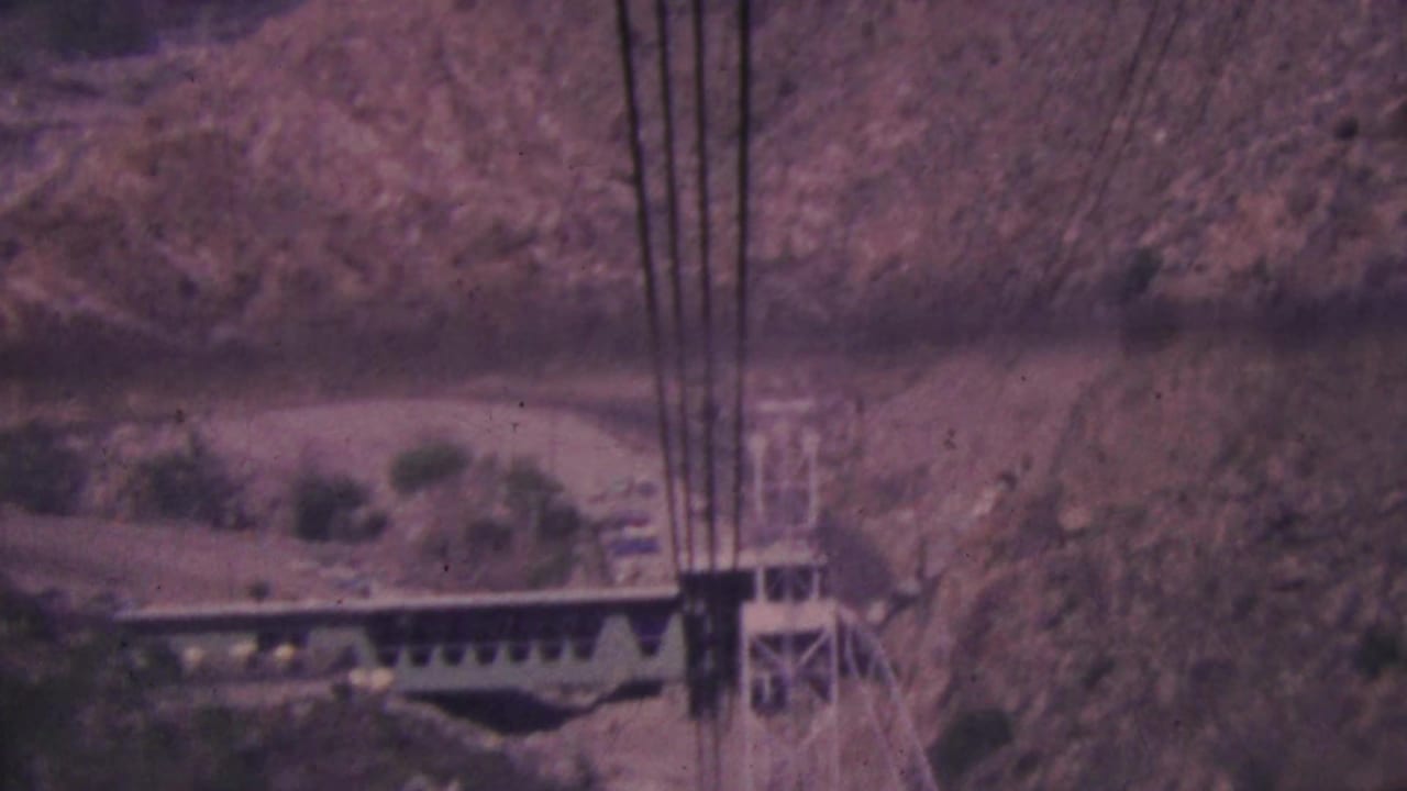 Aerial tramway cables and a tower appear against the rocky Palm Springs canyon terrain in soft, faded 8mm color.