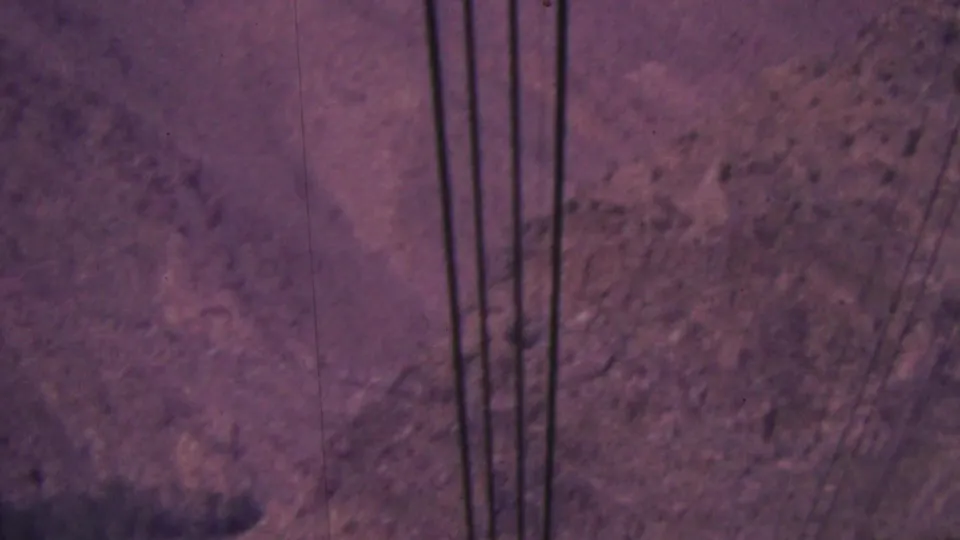 Faded 8mm frame from the Palm Springs tramway with dark cables cutting across a soft, rocky canyon background.