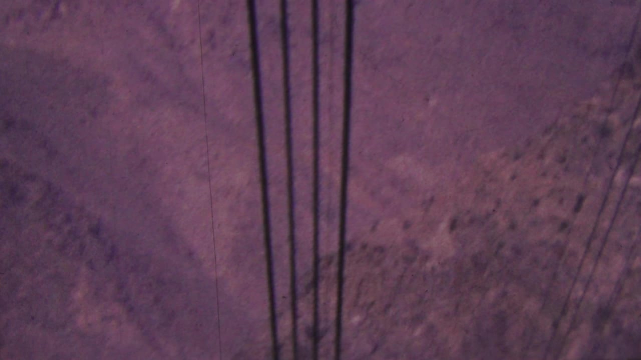 1964 Palm Springs 8mm frame showing dark vertical utility lines against a dry rocky mountainside with scattered shrubs.