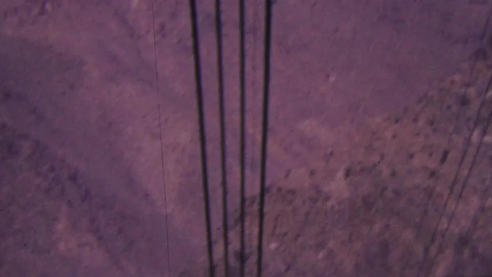 1964 Palm Springs 8mm frame showing dark vertical utility lines against a dry rocky mountainside with scattered shrubs.
