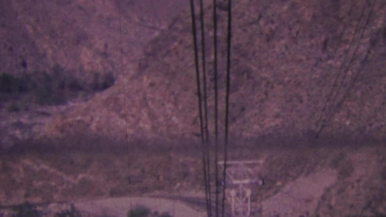 Power lines and a distant metal tower appear over a rugged hillside and road.