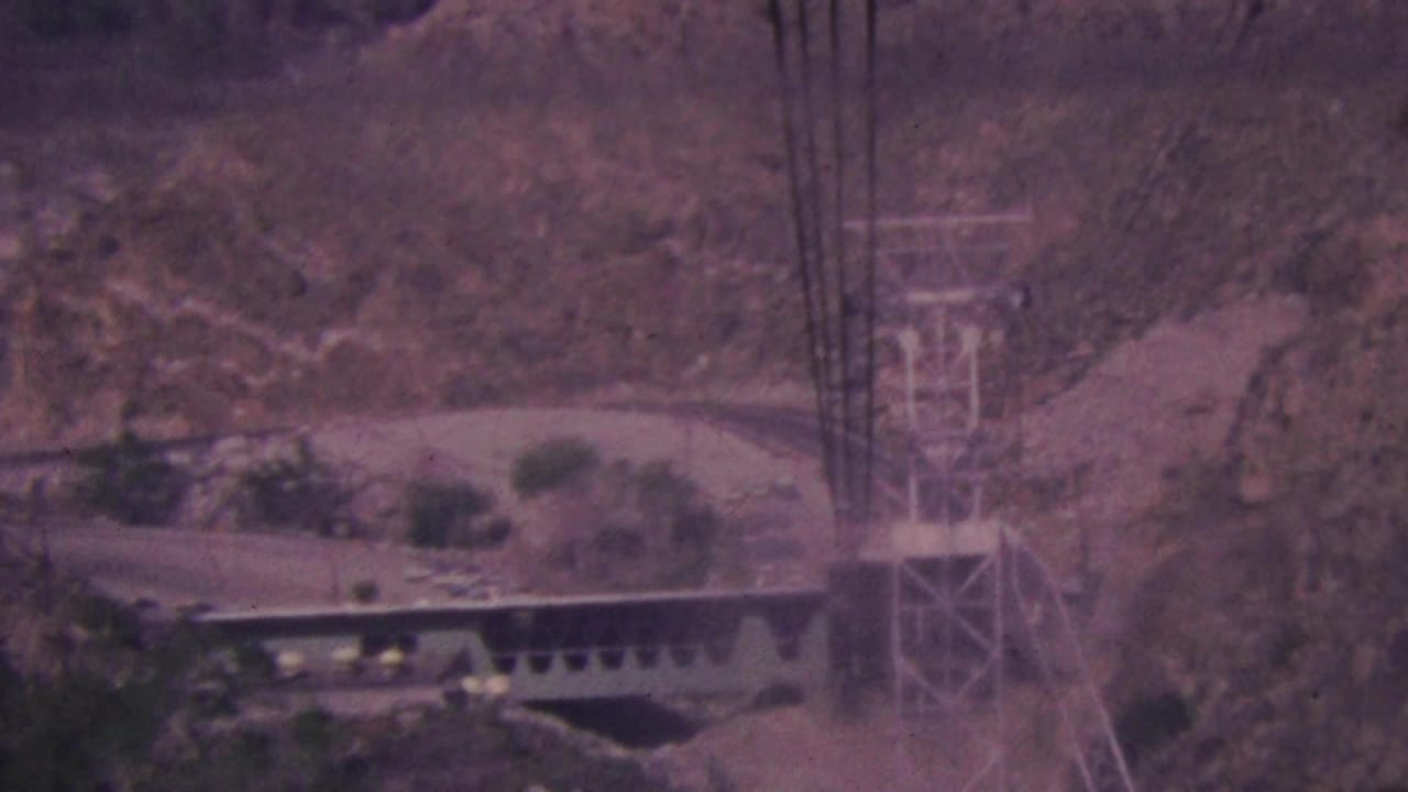 Distant tramway structures and support towers set against rocky desert canyon walls.