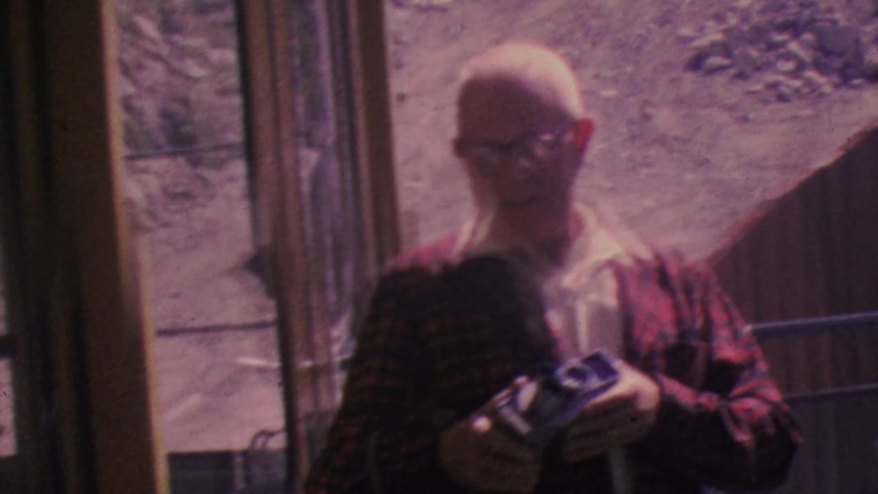Older man in a red plaid jacket holds a camera inside the tram car.