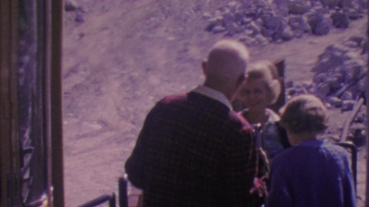 An older man and two women face one another near the tram entrance and railing.