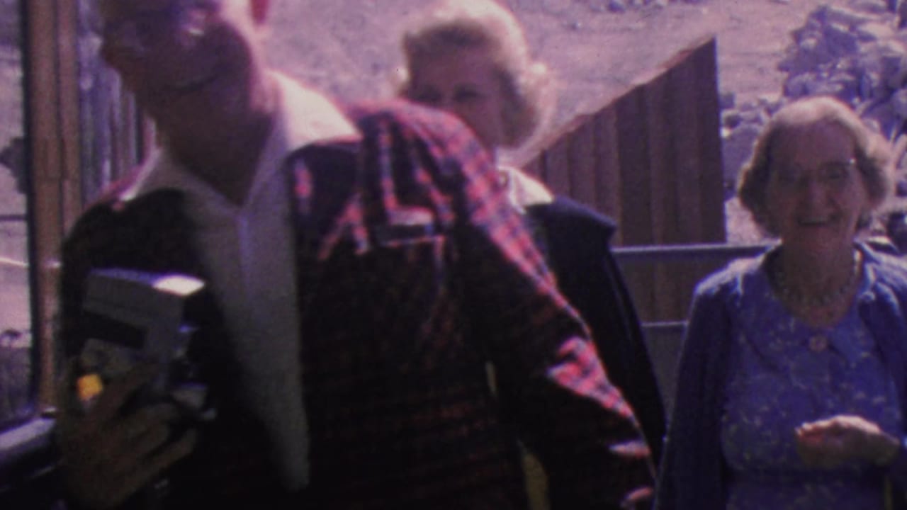 Older man holding a camera leans near the tram entrance as two women smile behind him.