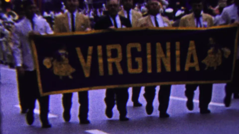 The large VIRGINIA banner passes close to the camera in the 1963 Indiana parade, with multiple adult marchers and spectators visible behind it.