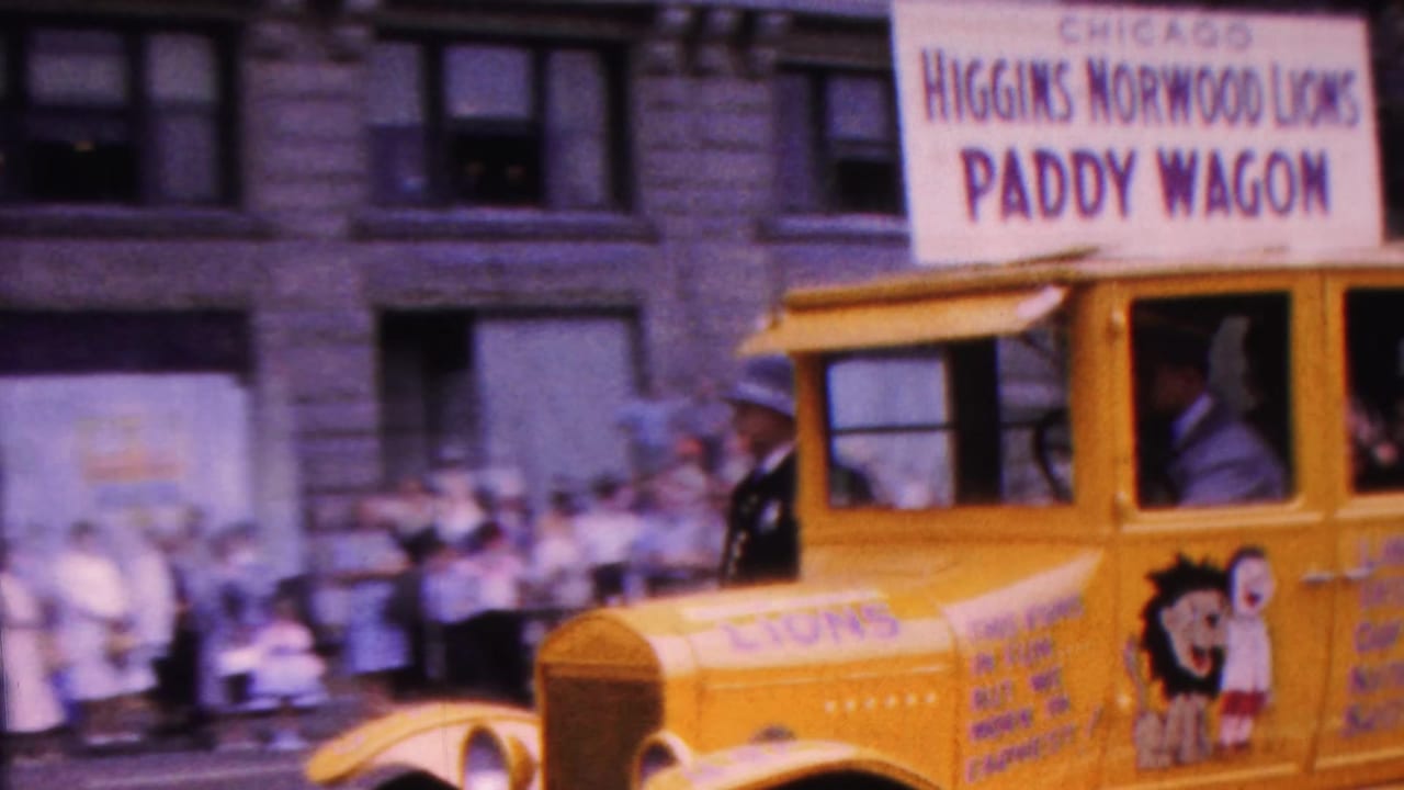 Yellow Higgins Norwood Lions Club paddy wagon float passing spectators on a city street.