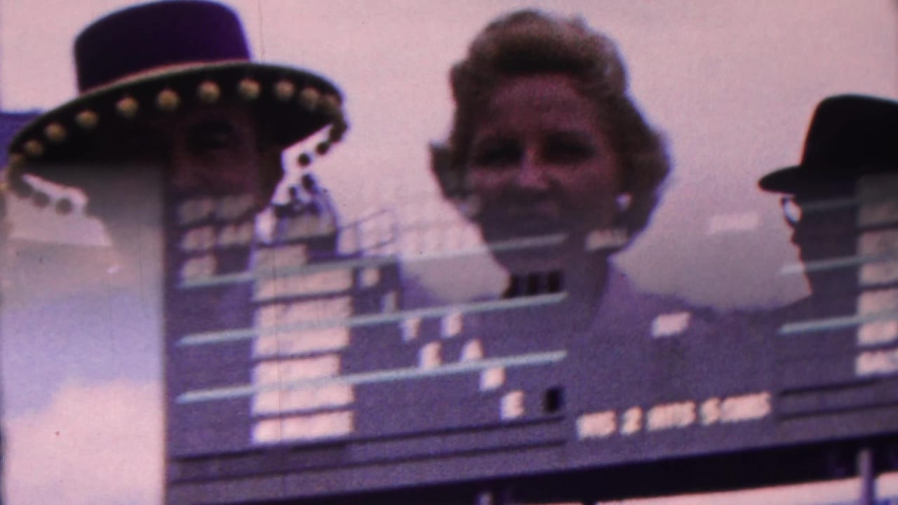 1963 Indiana 8mm frame showing a baseball scoreboard partly obscured by a double exposure or reflection of an adult face and a wide-brimmed hat silhouette.