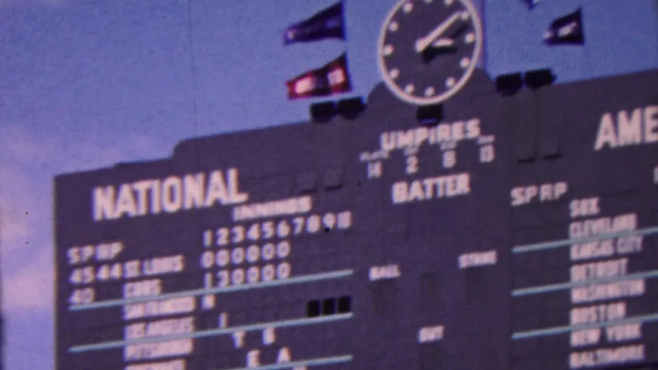 1963 Indiana 8mm frame showing a wider scoreboard view with an analog clock, small flags, National League listings, and part of the American League panel.