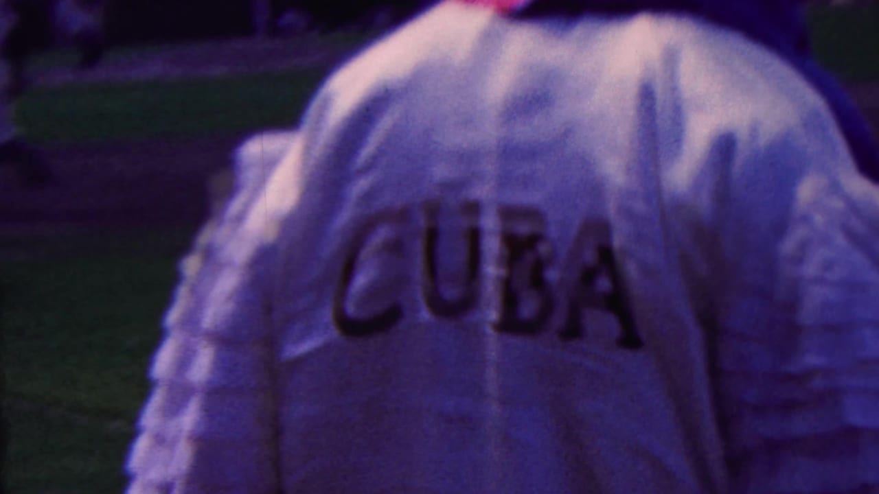 Close handheld 1963 8mm frame in Indiana showing the back of a white baseball uniform with large CUBA lettering near a stadium or field.