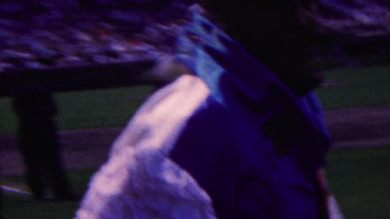In 1963 Indiana 8mm footage, a close foreground figure partly blocks a baseball field while players and a crowd are visible beyond.