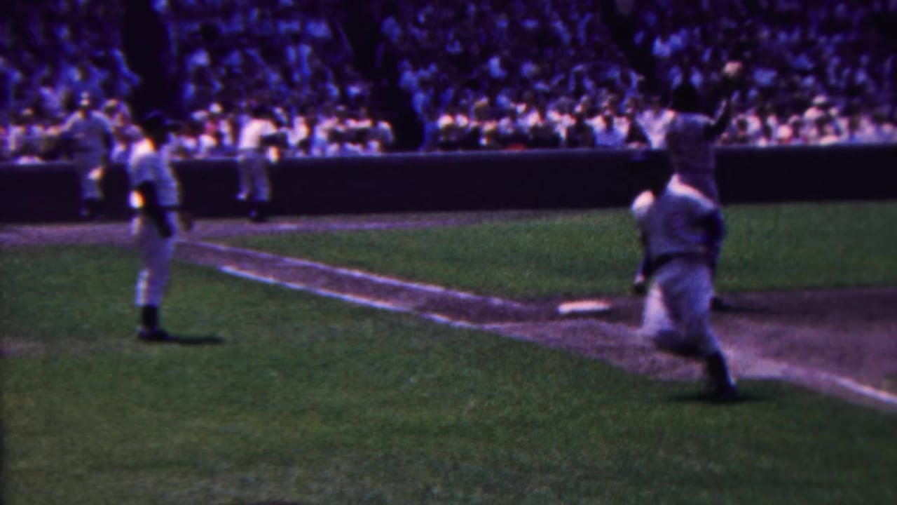 A baseball player runs along the baseline while another player stands on the field.