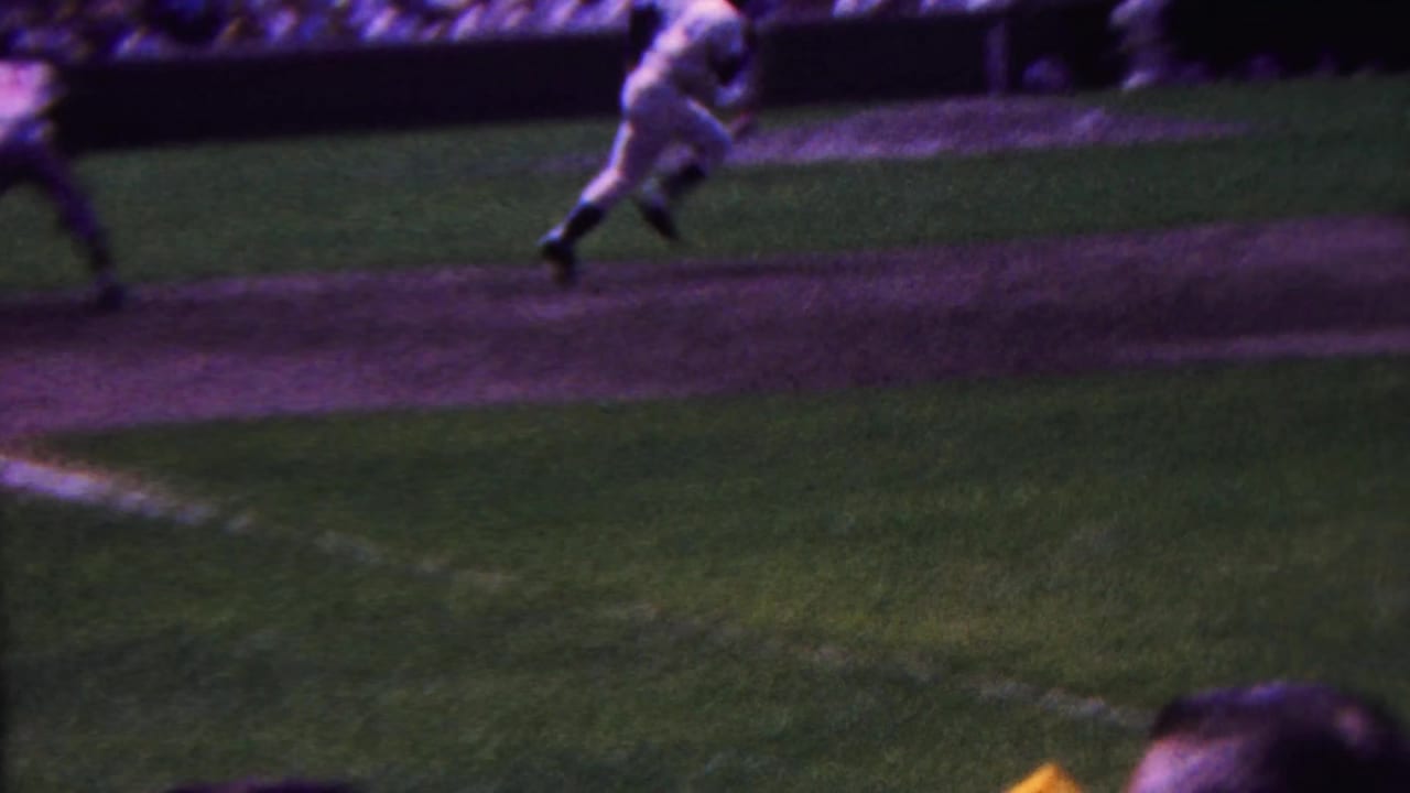 In 1963 Indiana home-movie footage, a baseball player in a white uniform appears to sprint along the baseline with bleachers visible in the background.