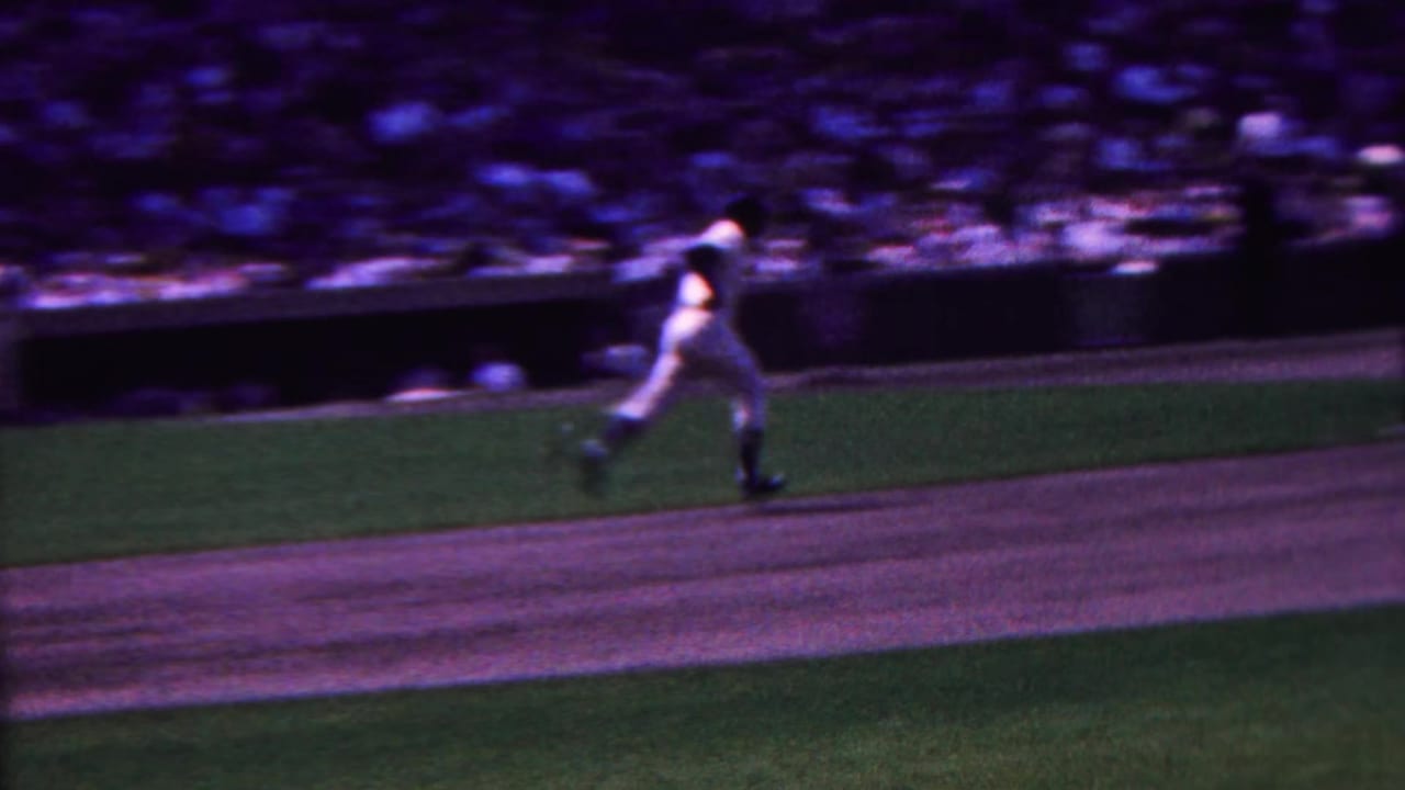 Player in a white baseball uniform runs across the field with the crowd blurred behind him.