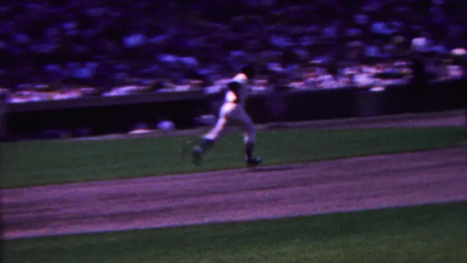 A white-uniformed baseball player runs across the grass and dirt in a 1963 Indiana ballgame scene, with spectators filling the distant stands.