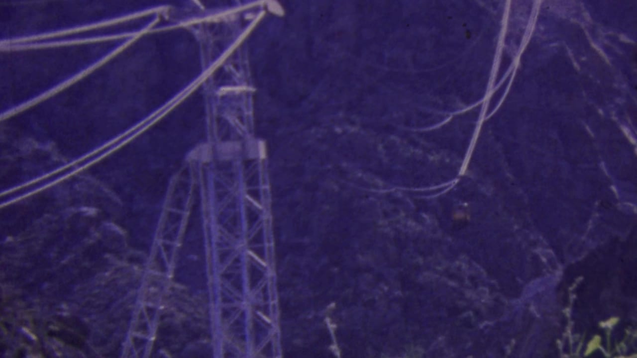 Tramway support tower and cables seen against a wooded mountain slope.