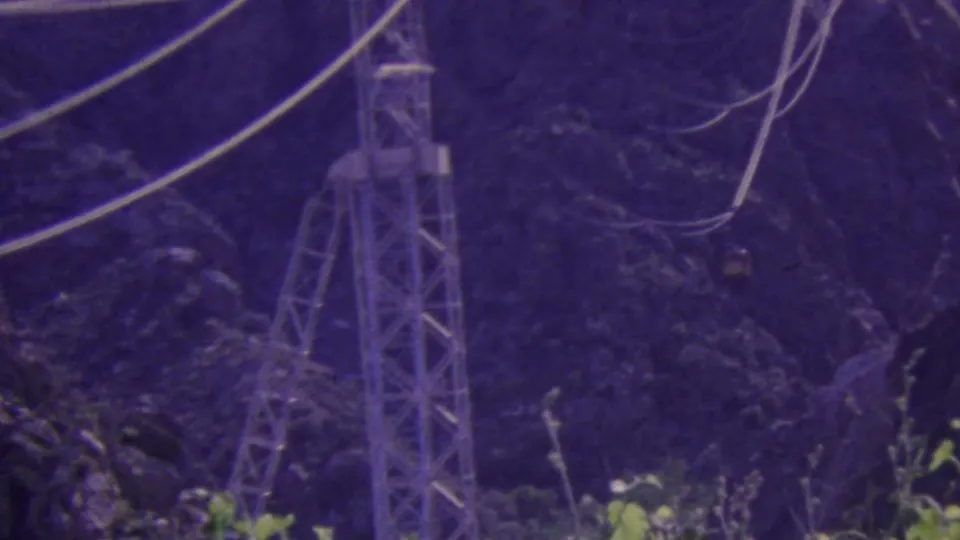 A purple-shifted 8mm frame shows the Palm Springs Aerial Tramway support tower and cables crossing a rocky, tree-covered mountain landscape.