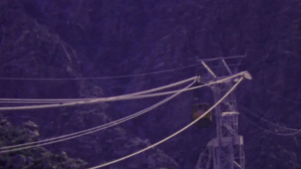 A small aerial tram car travels along the cable span beside a steel tower, with the Palm Springs mountain backdrop rendered in saturated home-movie color.