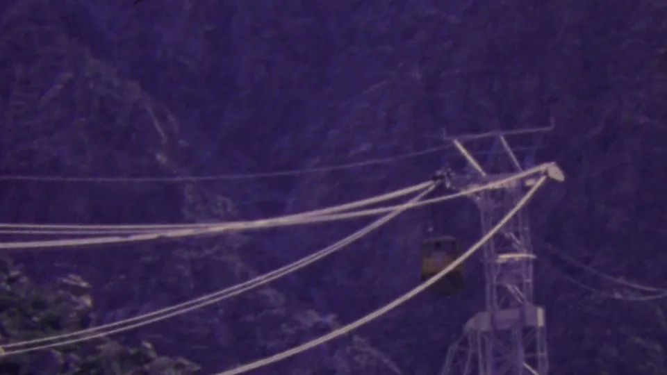 1964 Palm Springs Aerial Tramway view with a yellow tram car crossing steel cables near a support tower on a rugged mountain backdrop.