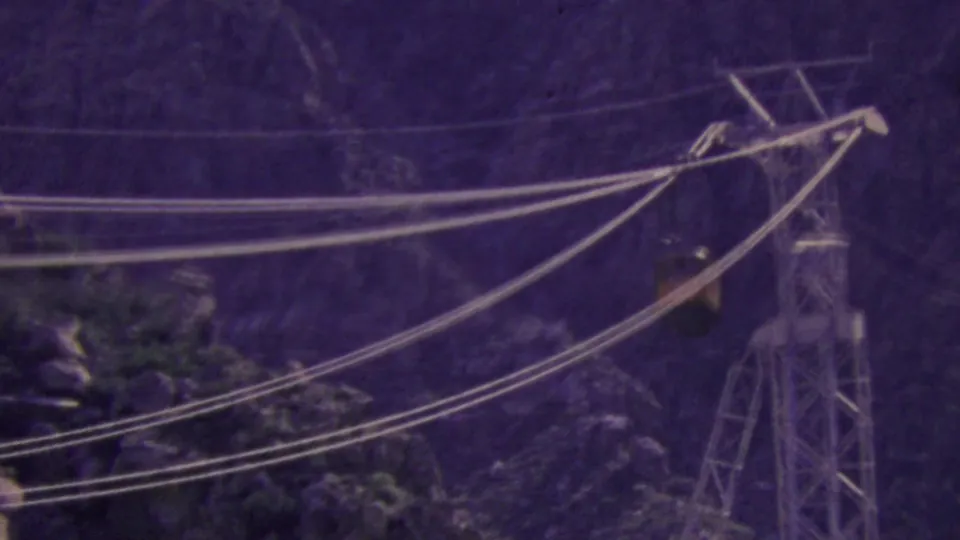 Palm Springs aerial tram cables span the rocky mountain scene, with a support tower visible at right and the small tram car partly obscured by distance and grain.
