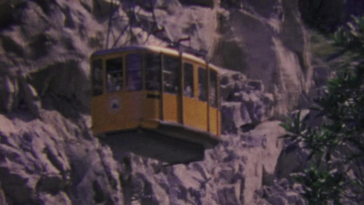 A yellow Palm Springs aerial tram cabin appears suspended near the rocky mountain wall, with passenger shapes visible behind the window glass.
