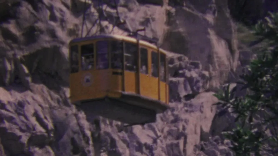 A yellow Palm Springs aerial tram cabin appears suspended near the rocky mountain wall, with passenger shapes visible behind the window glass.