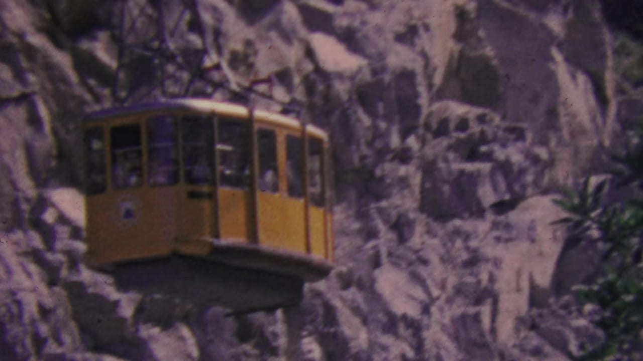 Close view of the yellow tram cabin crossing in front of pale rocks and foliage.