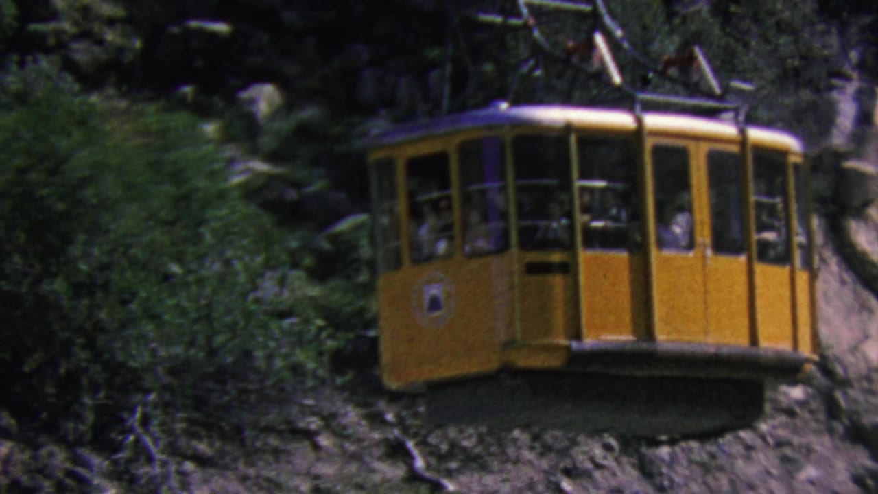 Yellow aerial tramway cabin in Palm Springs, California, seen in 1964 home-movie footage gliding past rocky terrain with passengers visible through the windows.