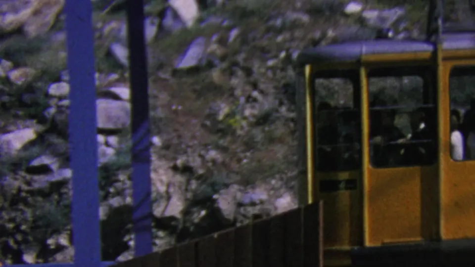 The yellow Palm Springs gondola fills the right side of the frame, with seated passengers visible through the windows and rocky mountain vegetation behind it.