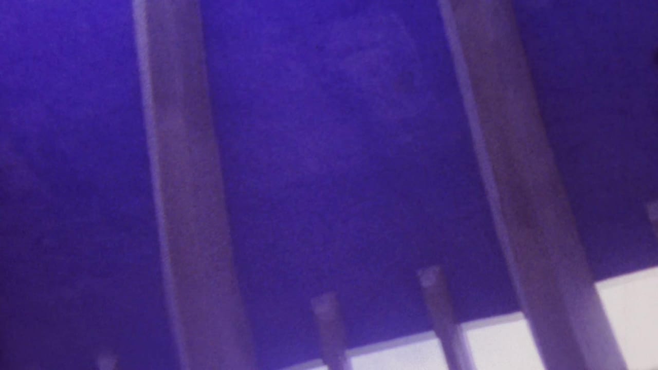 1964 Honolulu 8mm frame looking upward beneath bridge or elevated roadway supports, with dark pillars, pale beam edges, and strong violet-blue film color shift.