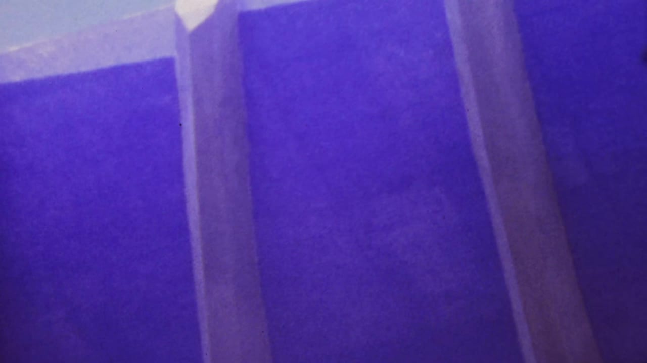 Low-angle 1964 Honolulu home-movie view beneath a bridge or elevated roadway, showing concrete pillars, underside beams, and pale sky openings through a blue-violet 8mm scan.