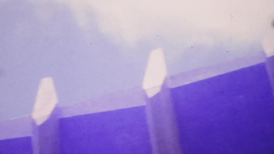 1964 Honolulu 8mm frame from below a bridge or elevated roadway, with two supports reaching into a bright sky area and heavy purple-blue film coloration.