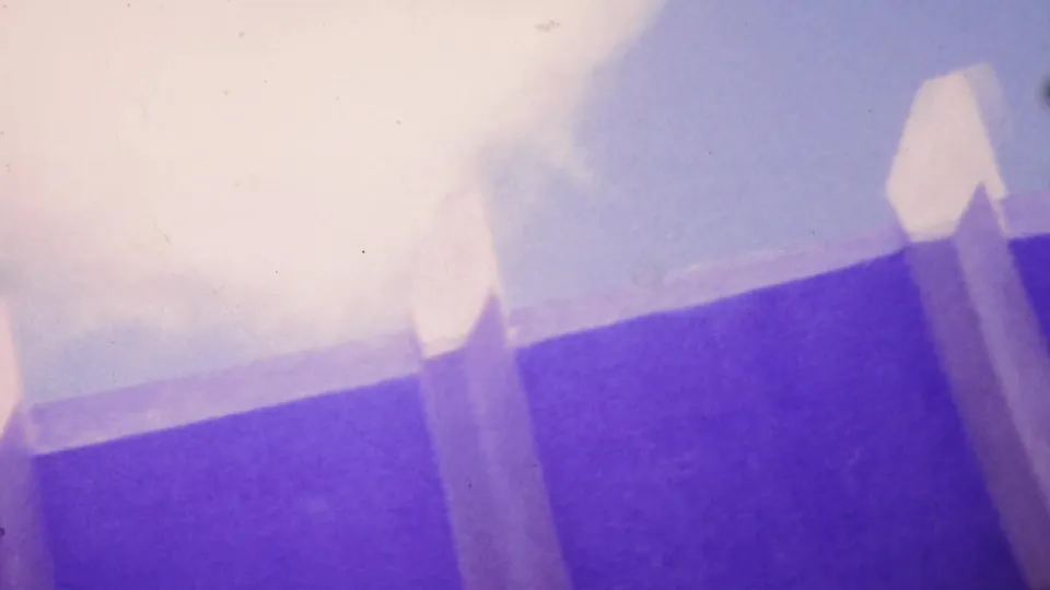 Low-angle 1964 Honolulu home-movie frame showing a prominent bridge or elevated roadway support, pale overhead edge, bright sky, and saturated violet-blue film texture.