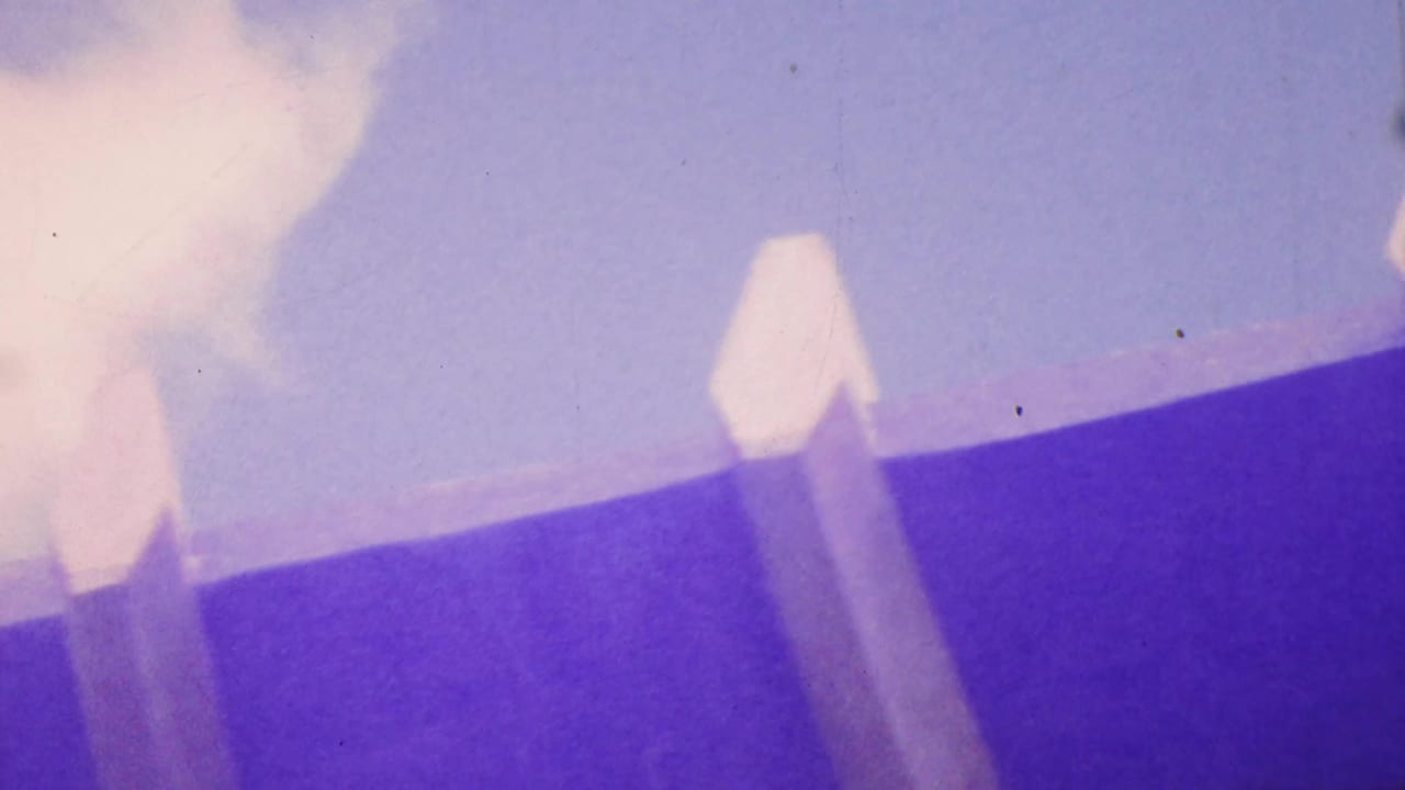1964 Honolulu 8mm frame showing a pale barrier or railing from a low angle against a purple-blue sky, with soft focus and color-shifted film texture.