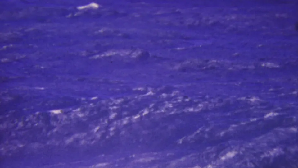 1964 Honolulu 8mm frame showing rough ocean texture and white streaks across the water, rendered with heavy blue-purple color shift and grain.