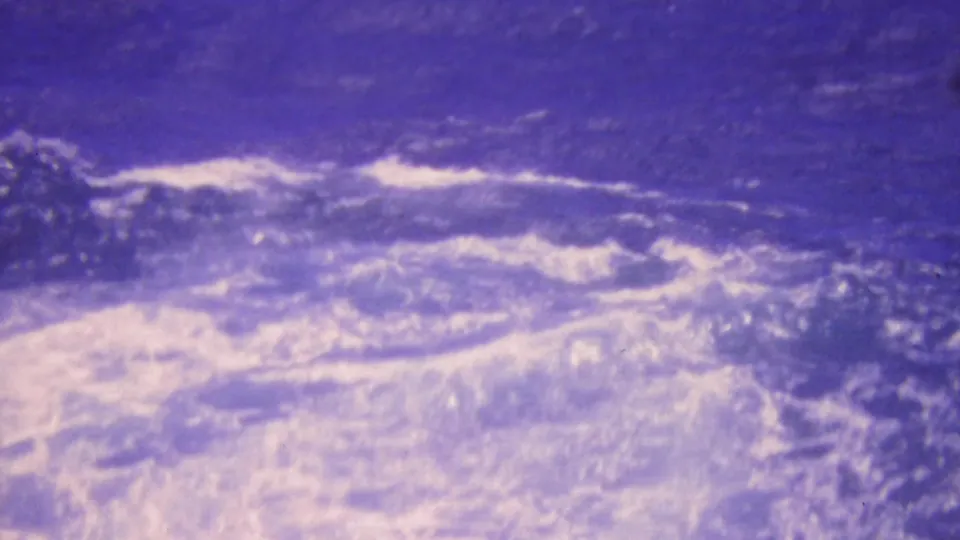 1964 Honolulu 8mm frame showing a brighter patch of foamy surf or breaking water amid dark blue ocean, with pronounced archival color shift and softness.