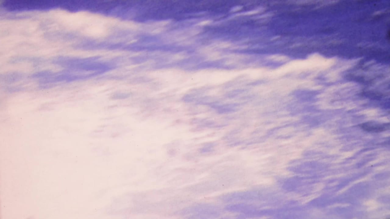 1964 Honolulu home-movie frame showing white-capped water moving along a dark rocky shoreline with strong purple-pink film shift.