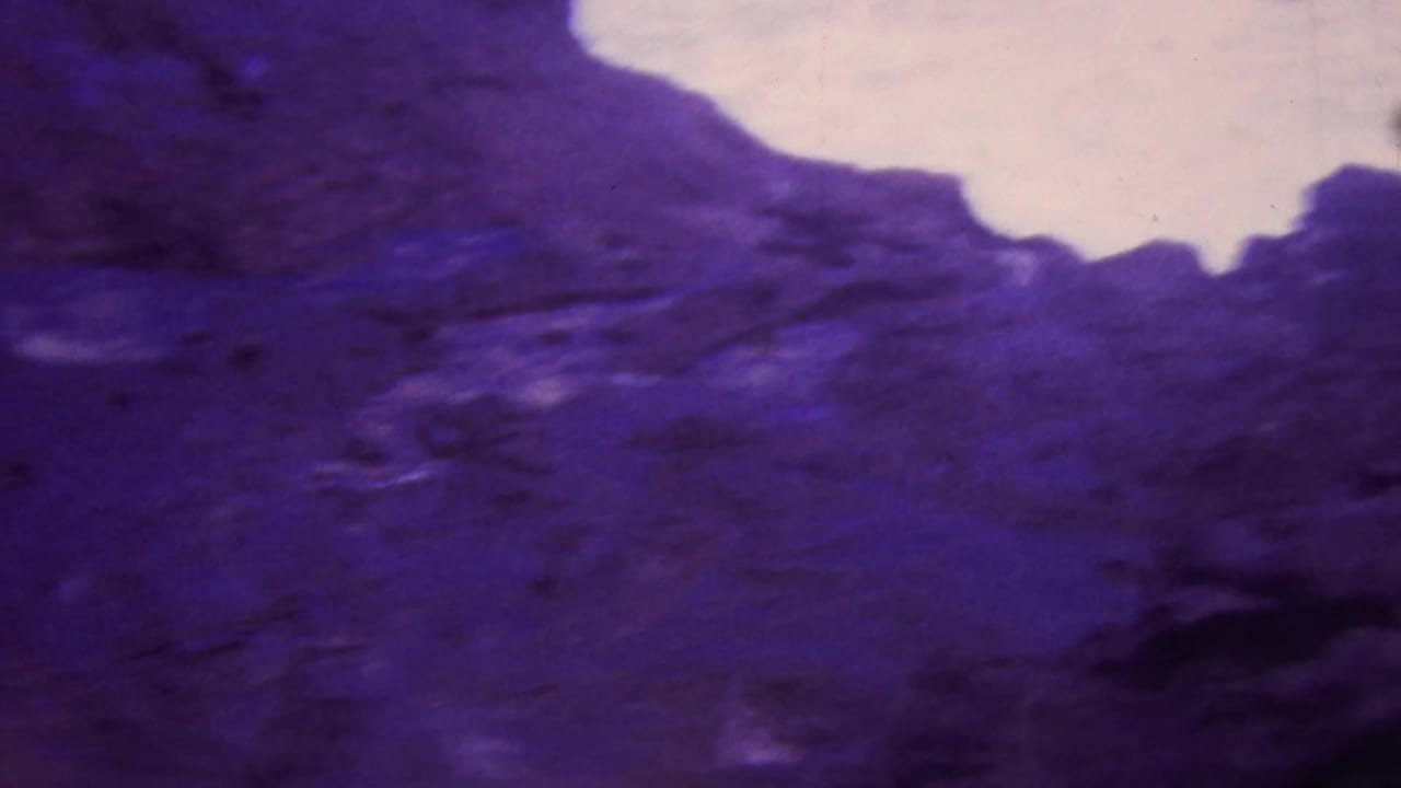 1964 Honolulu-area 8mm frame showing purple-shifted rugged rock formations with pale sky visible through the upper gap.