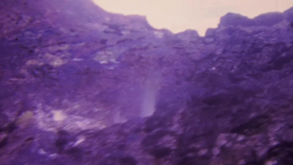 1964 Honolulu frame showing a soft, slightly blurred view of water moving through dark rocks, with visible grain and magenta-purple color degradation.