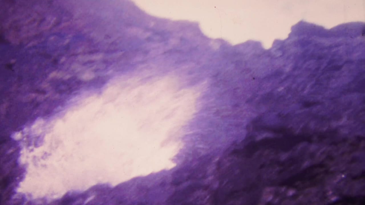 1964 Honolulu 8mm frame showing white ocean foam striking dark rocky shoreline under a strong purple-pink aged-film cast.