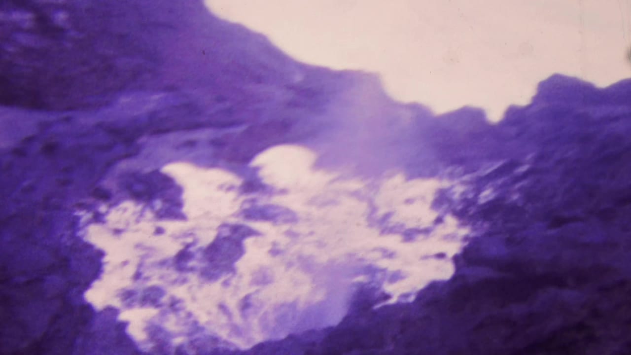 Churning white water gathers below dark coastal rocks.