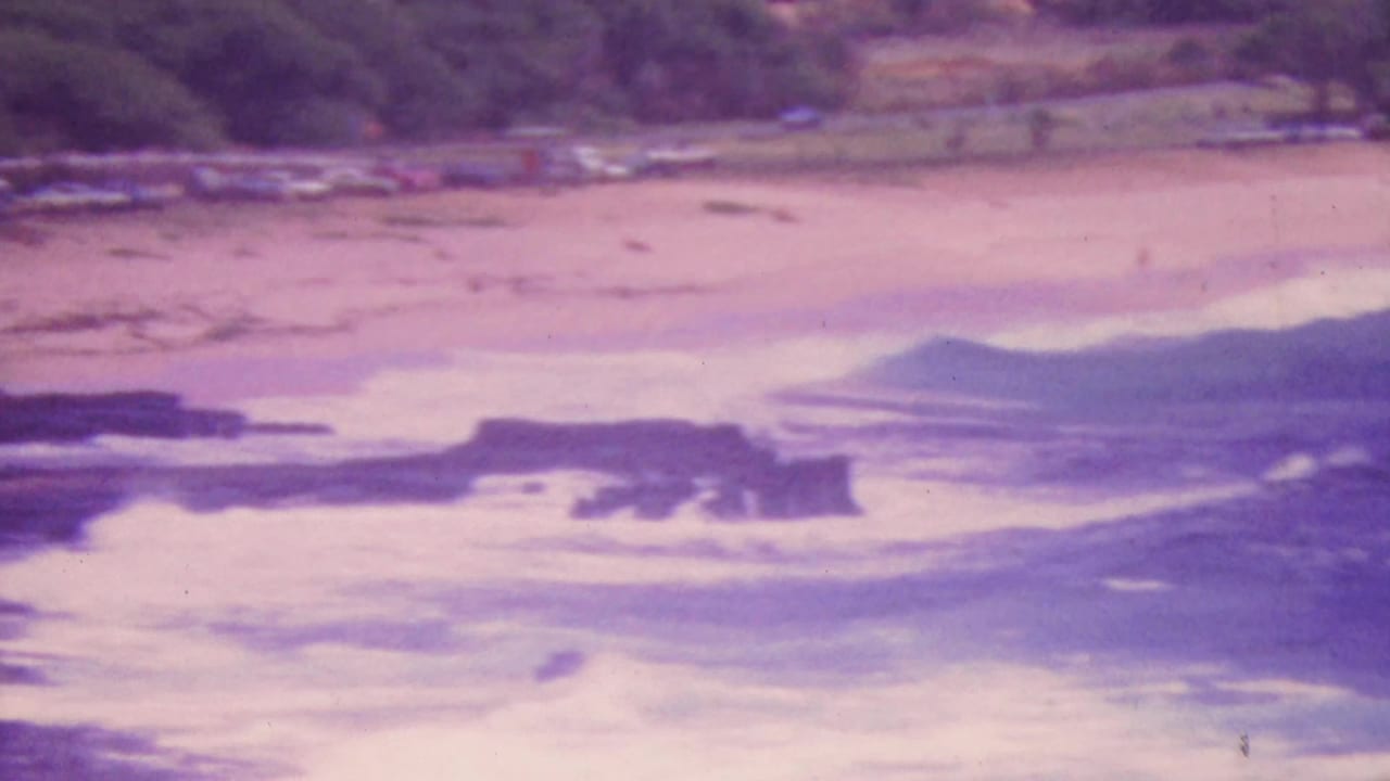 Soft, color-shifted 1964 8mm view of waves moving over a rocky reef along the Honolulu coast.