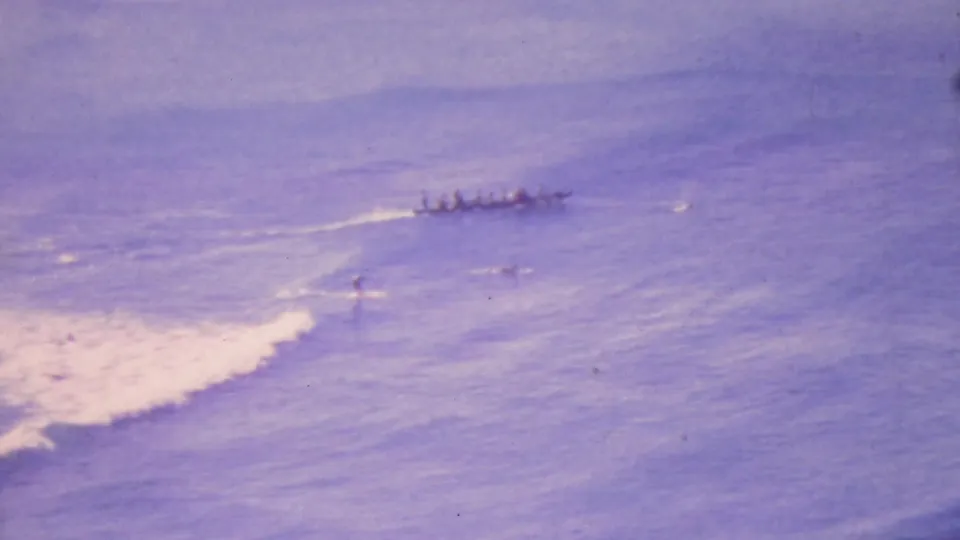 Wide 1964 8mm Honolulu ocean view with a small boat offshore and a lone surfer near foamy surf.