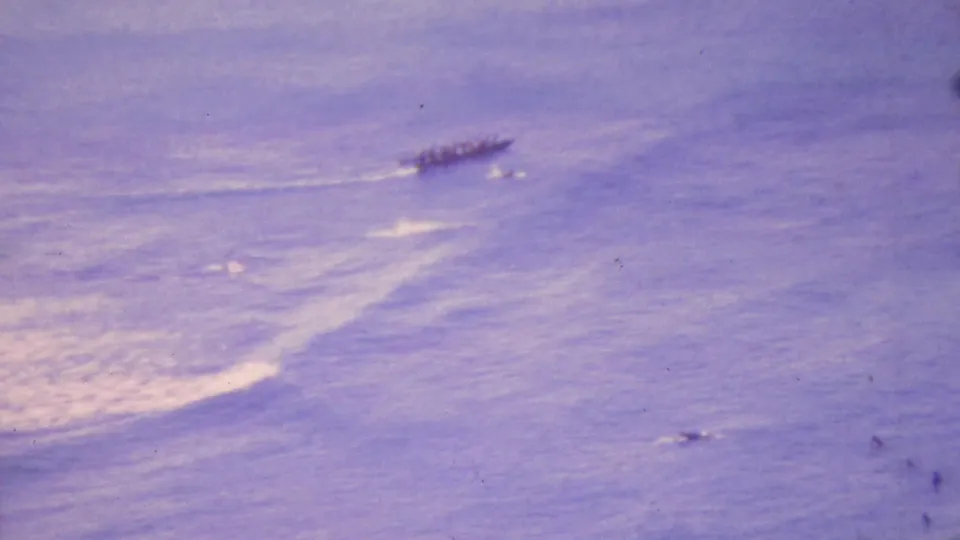 A distant outrigger canoe with paddlers appears above a patch of breaking surf, framed through soft, faded 8mm home-movie imagery from Honolulu in 1964.