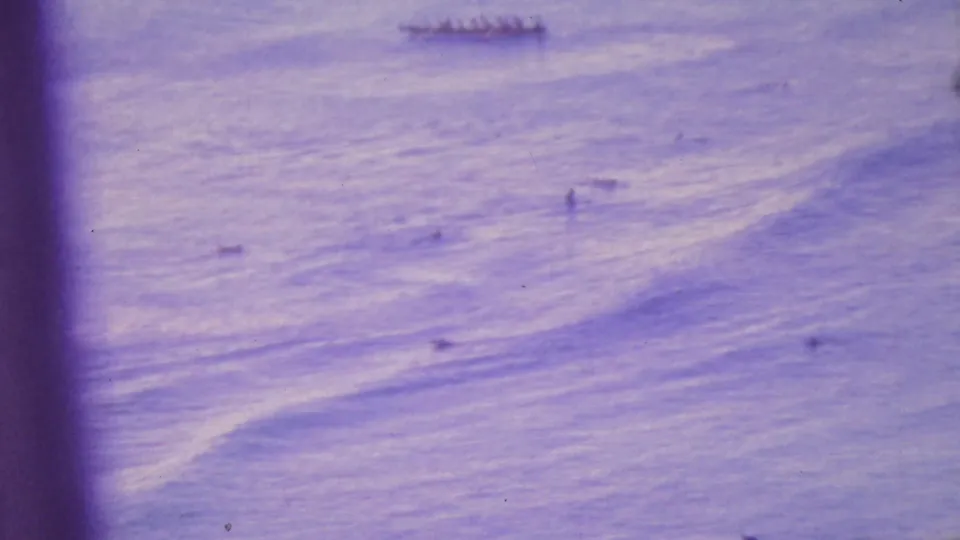 The canoe is partly distant near the upper frame while small water users appear below, with a dark vertical film or camera obstruction crossing the center of the 8mm frame.