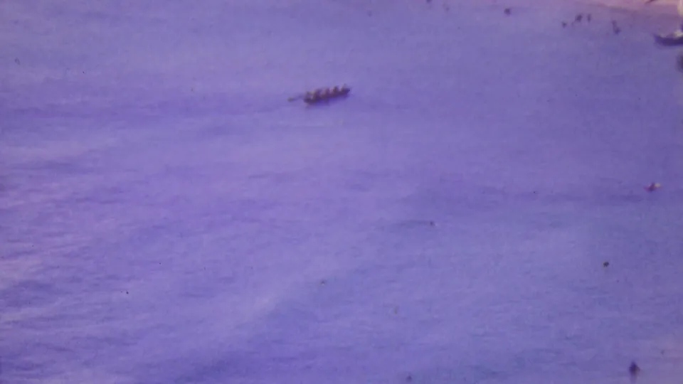 1964 Honolulu home-movie frame showing distant small canoe-like boats on open ocean with a strong purple-blue film cast.