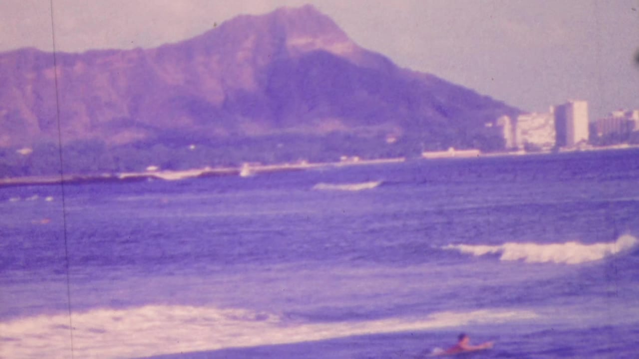 Diamond Head across the ocean with surf and distant shoreline buildings.