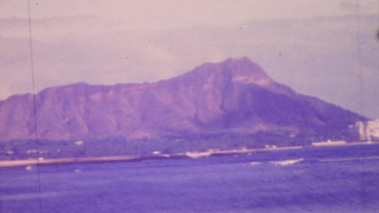 1964 Honolulu home-movie frame showing Diamond Head across the water with shoreline buildings and a soft, slightly faded 8mm color look.