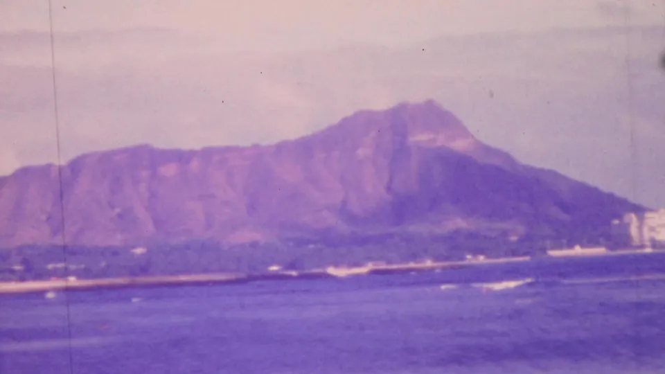 1964 Honolulu home-movie frame showing Diamond Head across the water with shoreline buildings and a soft, slightly faded 8mm color look.